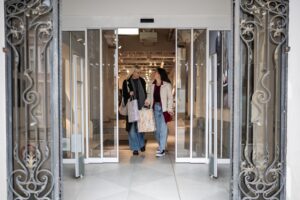 Two women with shopping bags in hand walking through automatic shop doors