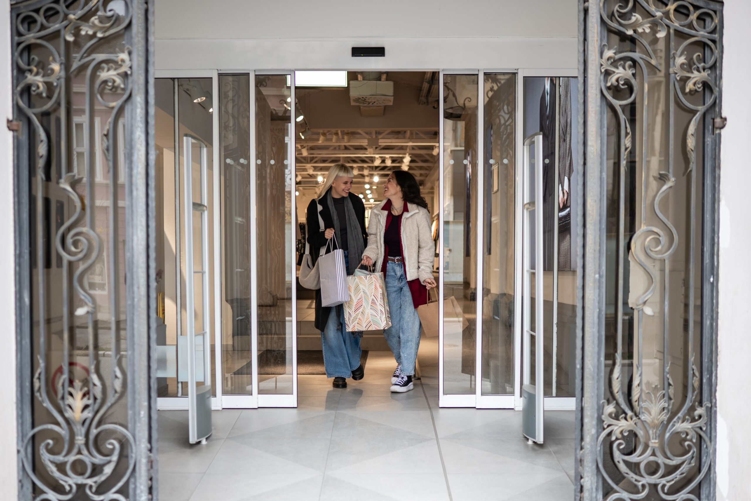 Two women with shopping bags in hand walking through automatic doors
